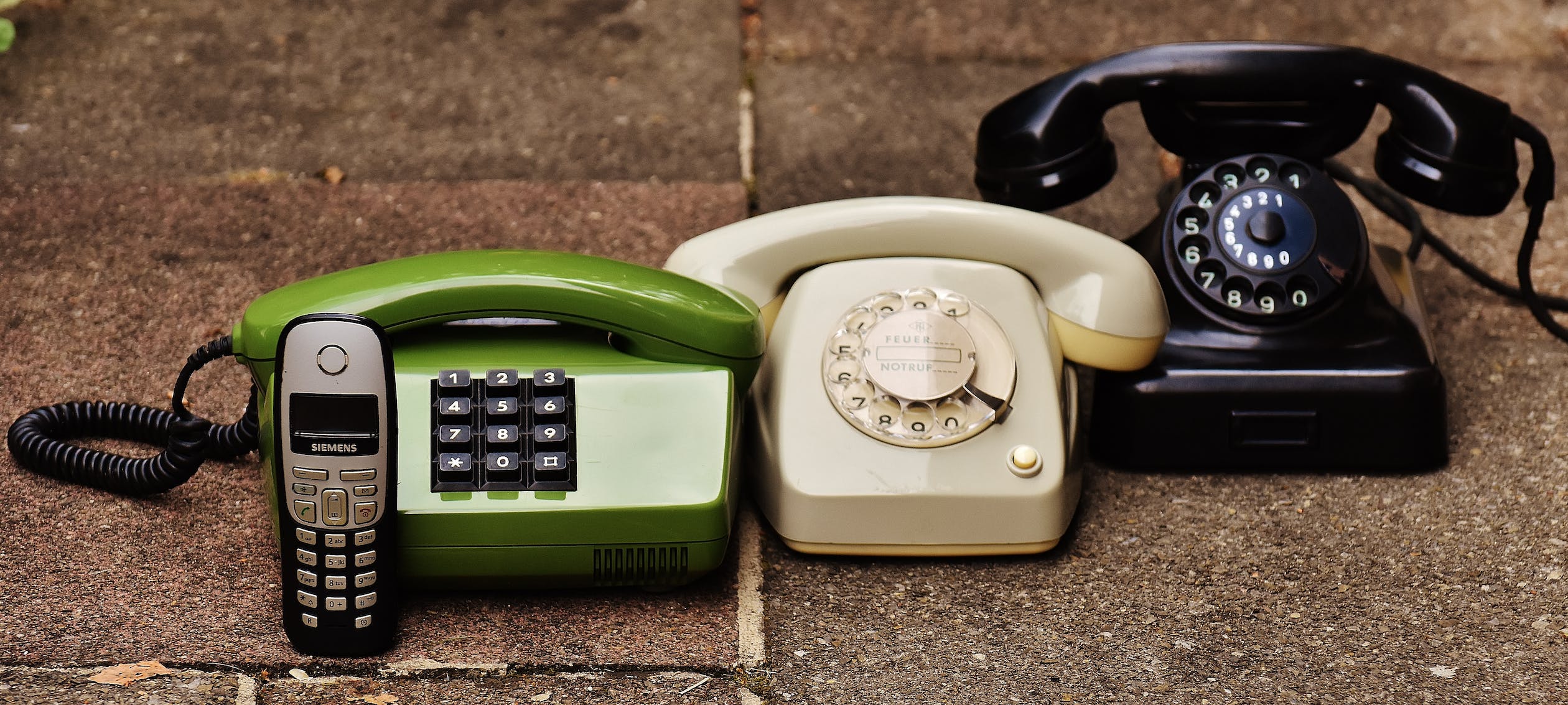 Image of an old candy-bar style phone, with several old-style landline phones.